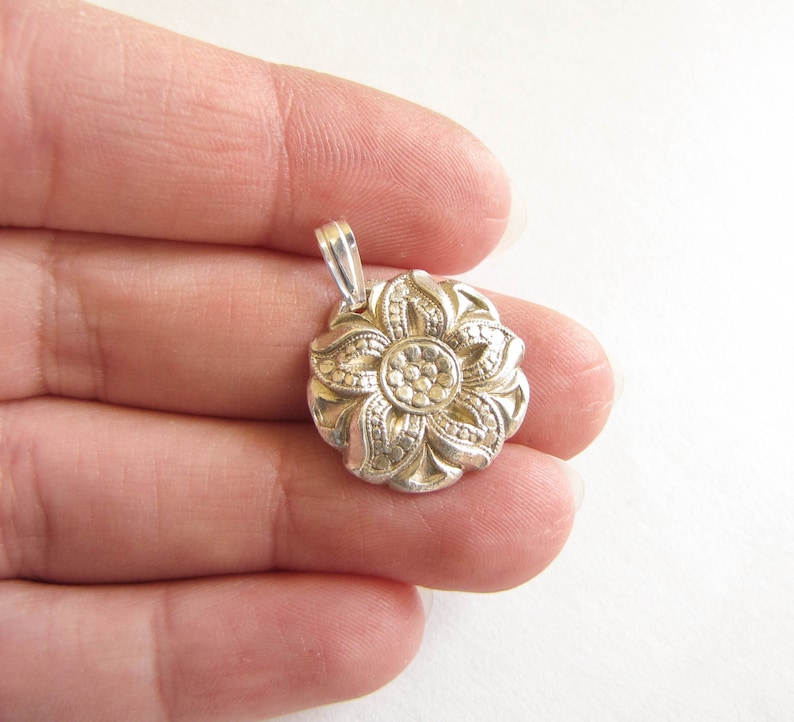 Puede incluir: Pendiente de plata en forma de flor con un dise&ntilde;o detallado. La flor tiene cinco p&eacute;talos y un centro con un patr&oacute;n circular.
