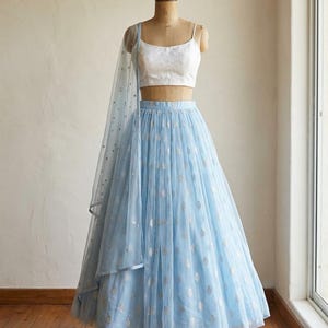 May include: A light blue skirt and top set on a mannequin. The skirt is a flowing tulle with silver leaf-like patterns. The top is white with thin straps. A matching sheer scarf drapes over the shoulder.