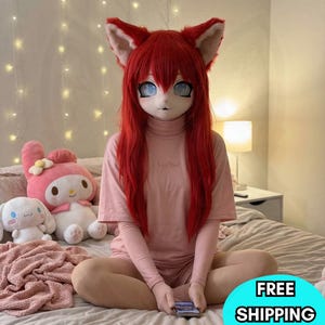 Puede incluir: Una persona con una máscara de orejas de zorro rojo con cabello rojo a juego, una camiseta rosa de cuello alto y pantalones cortos. La persona está sentada en una cama con peluches. El texto "FREE SHIPPING" está incluido.