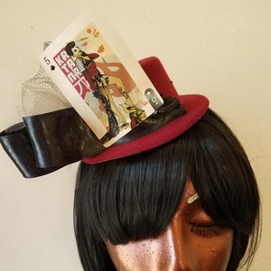 May include: A red felt top hat with a black ribbon and a white card with a woman in a red dress and the text "KATANA" on it.