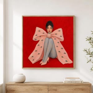 Può includere: Un dipinto quadrato incorniciato su sfondo rosso raffigurante una persona dai capelli scuri seduta con le ginocchia raccolte, che indossa collant grigi e tacchi rosa, avvolta in un grande fiocco rosa pallido decorato con numerosi occhi realistici.