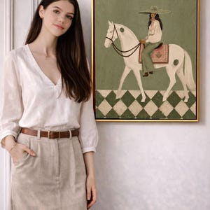 May include: A framed wall art print featuring a painting of a person wearing a wide-brimmed hat and light-colored clothing, riding a white horse. The horse stands on a green and white checkered floor against a solid sage green background.