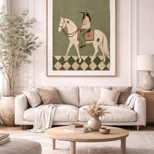 May include: A framed wall art print featuring a painting of a person wearing a wide-brimmed hat and light-colored clothing, riding a white horse. The background is sage green with a checkered pattern at the bottom in dark green and white.