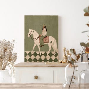 May include: A rectangular wall art print featuring a painting of a person wearing a wide-brimmed hat and light-colored clothing, riding a white horse. The horse wears a saddle with a pink patterned blanket. The background is olive green.