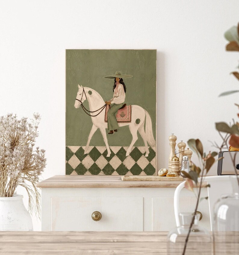 May include: A rectangular wall art print featuring a painting of a person wearing a wide-brimmed hat and light-colored clothing, riding a white horse. The horse wears a saddle with a pink patterned blanket. The background is olive green.