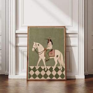 May include: A framed art print featuring a white horse with a rider wearing a wide-brimmed hat and light-colored clothing. The horse has a pink saddle blanket and dark reins. The background is olive green with a white and green diamond floor pattern.