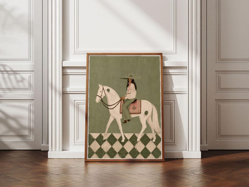 May include: A framed art print featuring a white horse with a rider wearing a wide-brimmed hat and light-colored clothing. The horse has a pink saddle blanket and dark reins. The background is olive green with a white and green diamond floor pattern.