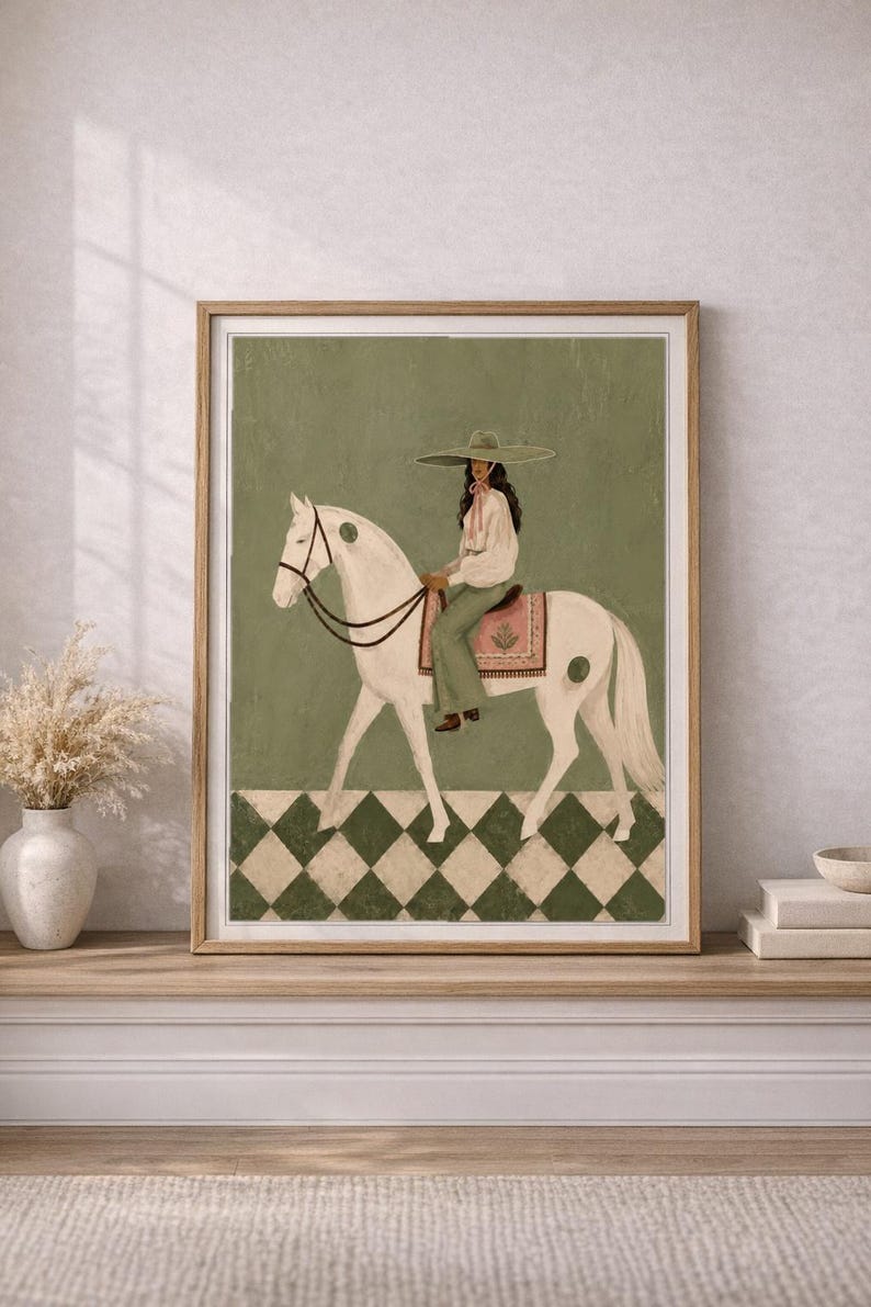 May include: A framed wall art print featuring a person wearing a wide-brimmed hat, a white blouse, and green trousers, riding a white horse. The horse has green circular markings and a pink saddle blanket. The background is green with a checkered floor.