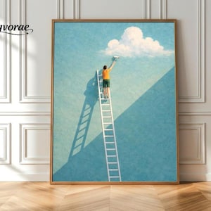 Puede incluir: Una impresión artística enmarcada representa a una persona en una escalera pintando una nube en un cielo azul. La persona lleva una camisa naranja y pantalones cortos verdes. La obra de arte tiene un marco dorado y está sobre una pared blanca y un suelo de madera.