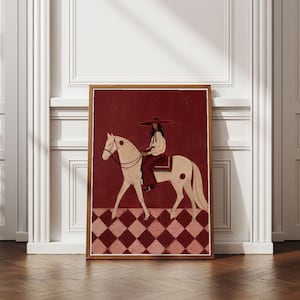 Può includere: Una stampa d'arte incorniciata raffigurante una persona con un cappello a tesa larga e abiti chiari, a cavallo di un cavallo color crema. Lo sfondo è rosso scuro e il primo piano presenta un pavimento con un motivo a rombi rossi e rosa.