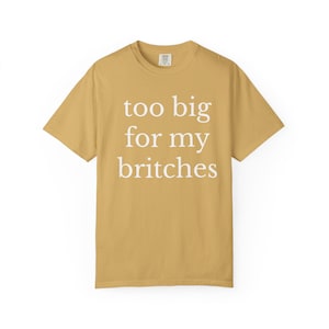May include: Mustard yellow t-shirt with the phrase "too big for my britches" printed in white. The shirt has a crew neck and short sleeves. The text is centered on the front of the shirt.