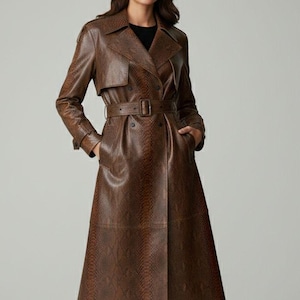 Może przedstawiać: Brązowy skórzany trencz z wzorem skóry węża. Płaszcz ma wiązany w talii pasek, dwurzędowy krój i długość do kostek. Modelka ma na sobie czarne buty. Stylowa opcja odzieży wierzchniej.