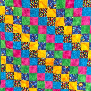 May include: A colorful patchwork quilt with a vibrant grid pattern. Squares of pink, green, yellow, and blue fabrics are arranged in a repeating pattern. Some squares feature patterned designs, including stars, kites, and abstract shapes. The quilt is a cheerful and decorative textile.