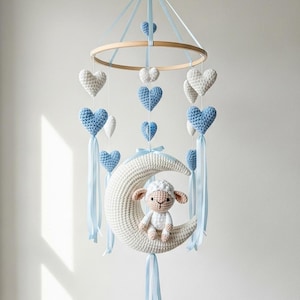 Op de afbeelding: Handgemaakte baby mobile met een houten ring, blauwe en witte gehaakte harten en een gehaakt lammetje op een halve maan. De mobile is opgehangen aan een berken tak met blauwe linten.