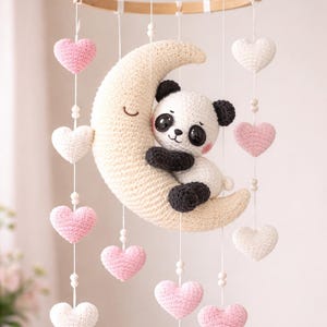 Peut inclure: Mobile pour bébé fait à la main avec un panda en crochet embrassant un croissant de lune crème. Des cœurs roses et blancs en crochet pendent de l'anneau en bois, créant une décoration de chambre d'enfant.