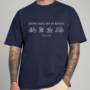 May include: Navy blue t-shirt with white text and line art illustrations. The text reads "KEINE ZEIT, BIN IN RENTE" above a bicycle, stroller, plant, and camper. Below the illustrations is "MAI 2026".