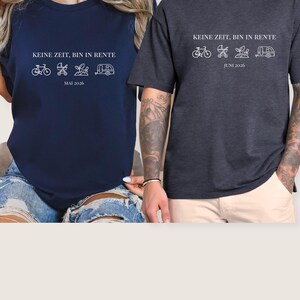 May include: Two dark-colored t-shirts with white text and graphics. The text reads "KEINE ZEIT, BIN IN RENTE" above a bicycle, stroller, plant, and camper graphic. One shirt says "MAI 2026" and the other says "JUNI 2026".