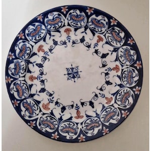 Peut inclure: Une assiette ronde en céramique blanche avec un motif floral bleu et orange. L'assiette présente une bordure bleu foncé avec des motifs floraux répétés et un motif floral central. Le design comprend des fleurs et des feuilles stylisées.