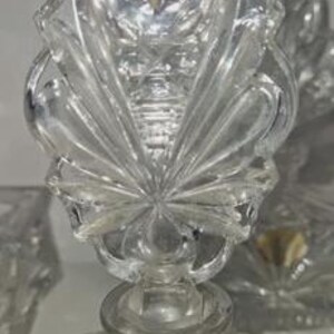 May include: Clear crystal perfume bottle with a decorative stopper. The stopper features a starburst design with a detailed, textured pattern. The bottle has a round base and a label that reads "Echt Leikristall Gepresst".