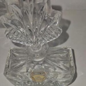 May include: A clear, faceted glass perfume bottle with a decorative, fan-shaped stopper. The rectangular base has a diamond pattern. A ruler is placed near the bottle. The bottle measures approximately 4 inches in height.