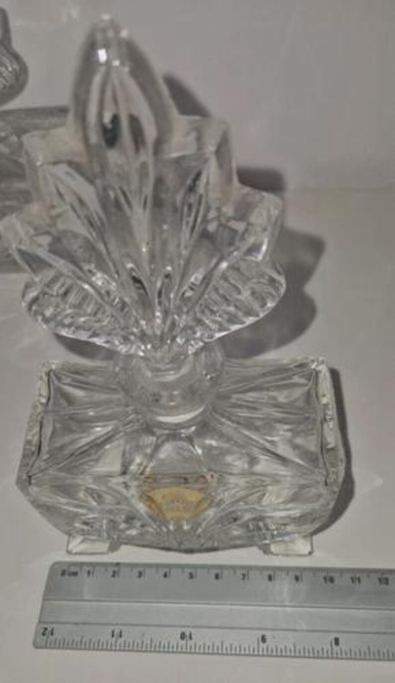 May include: A clear, faceted glass perfume bottle with a decorative, fan-shaped stopper. The rectangular base has a diamond pattern. A ruler is placed near the bottle. The bottle measures approximately 4 inches in height.