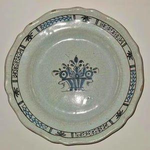 Könnte beinhalten: Ein weißer Keramikteller mit gewelltem Rand und blauem Blumendesign in der Mitte. Der Teller hat einen blau-weißen Rand mit geometrischen und floralen Mustern. Der Teller hat einen Durchmesser von etwa 23 cm.