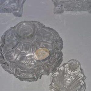 May include: Clear glass perfume bottles with intricate designs. One bottle is round with a floral pattern, and another has a rectangular shape. A decorative stopper is next to the round bottle. The bottles are empty and appear to be vintage.