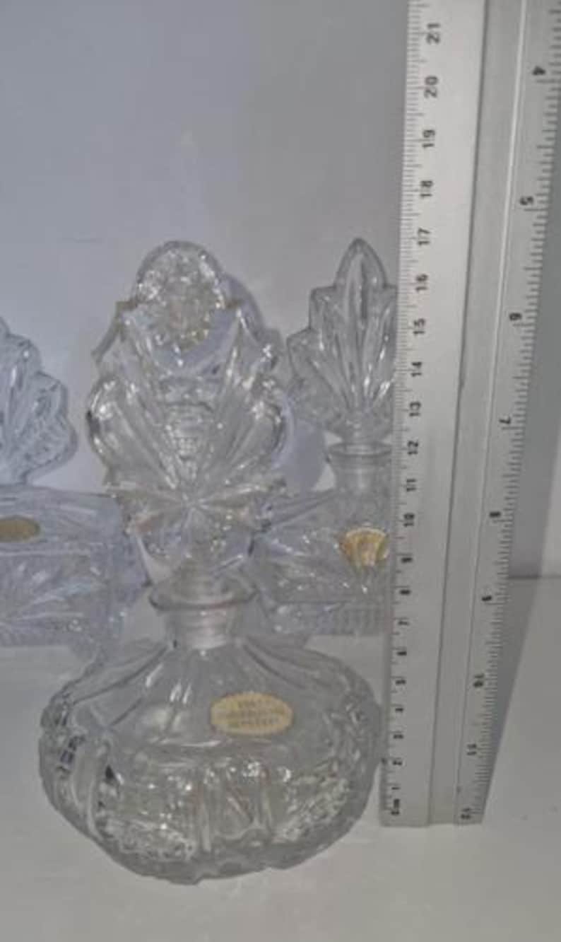 May include: Clear crystal perfume bottle with a round base and a decorative stopper. The bottle is approximately 5 inches tall. The stopper has a starburst design. The bottle has a label that reads "Made in Czechoslovakia".
