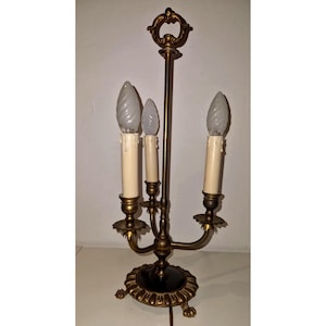 May include: An antique brass candelabra-style lamp with three faux candle lights. The lamp has a decorative base with a black center and ornate detailing. The lamp is approximately 20 inches tall.