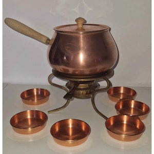 Peut inclure: Un service à fondue en cuivre avec une poignée et un couvercle en bois, posé sur un support en laiton. Comprend six petits bols à trempette en cuivre. Un ensemble classique pour les réceptions.