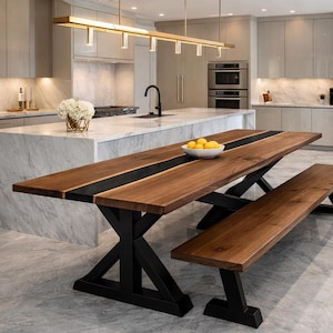 May include: A contemporary kitchen featuring a large wooden dining table and bench. The table has a dark wood top with a black stripe and black legs. A bowl of lemons sits on the table. The kitchen has stainless steel appliances and marble countertops.