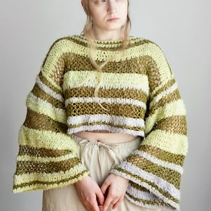 May include: A cropped, long-sleeved crochet jumper featuring horizontal stripes in shades of olive green, pale yellow, and light lavender. The garment has a loose, open-knit texture with wide, flared sleeves and a wide, rounded neckline.