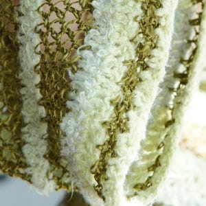 May include: A textile fabric featuring an alternating striped pattern of olive green open-weave mesh and textured, fuzzy cream-coloured yarn. The material displays a distinct contrast between the smooth, thin green threads and the soft, thick white fibres.