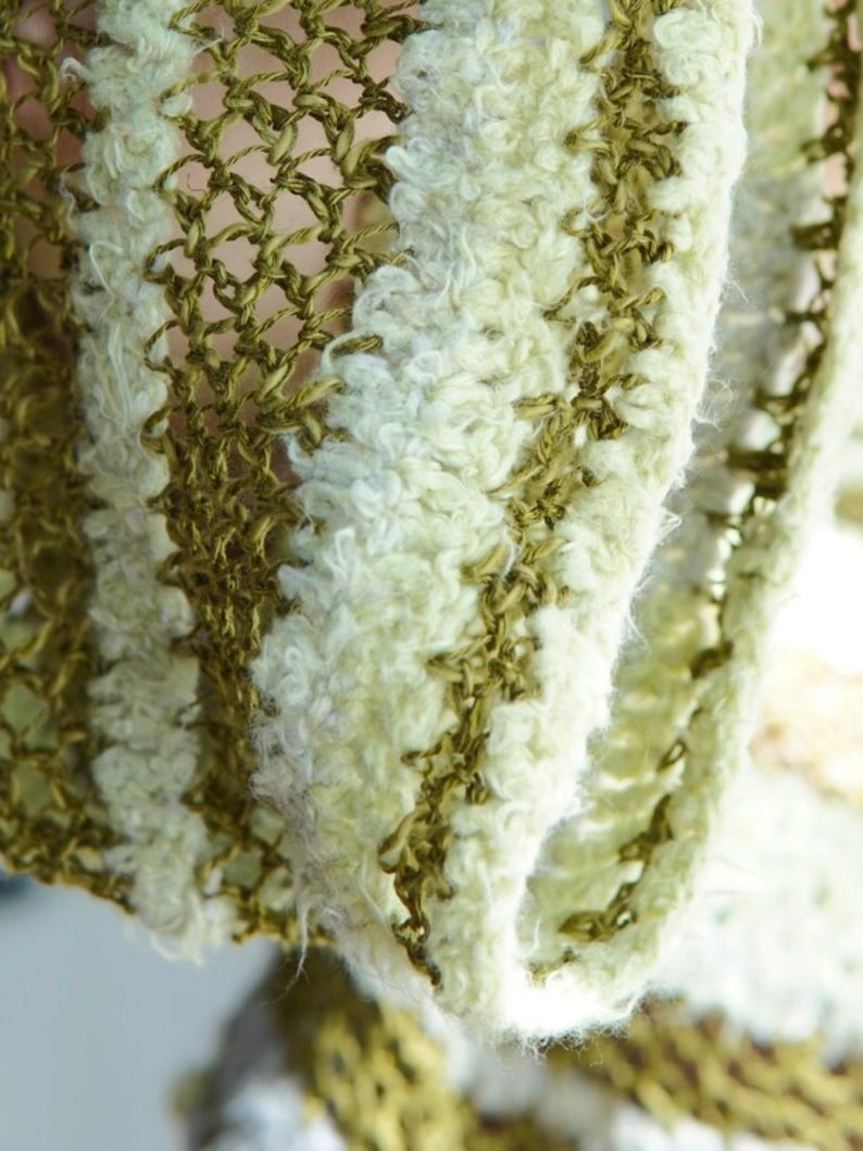 May include: A textile fabric featuring an alternating striped pattern of olive green open-weave mesh and textured, fuzzy cream-coloured yarn. The material displays a distinct contrast between the smooth, thin green threads and the soft, thick white fibres.