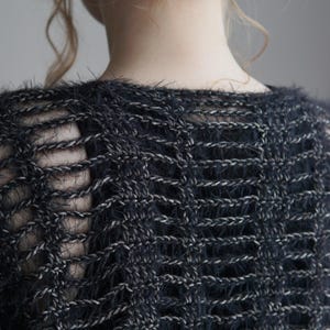 May include: A dark charcoal gray knit top featuring a loose, open-weave construction with a fuzzy, textured yarn. The garment displays a repeating vertical pattern of horizontal stitches, creating a semi-sheer effect across the back and shoulders.