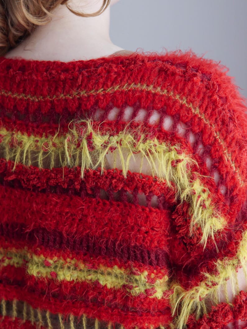 May include: A crochet sweater featuring horizontal stripes in vibrant red, deep burgundy, and bright lime green. The garment is constructed with a mix of textured, fuzzy yarn and open-work stitch patterns, creating a layered, multi-dimensional appearance.