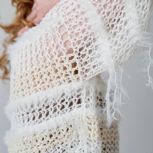 May include: A long-sleeved, open-knit jumper in cream and off-white tones. The garment features a loose, airy crochet-style weave with horizontal bands of fuzzy, textured yarn trim that add dimension to the lightweight, semi-sheer fabric.