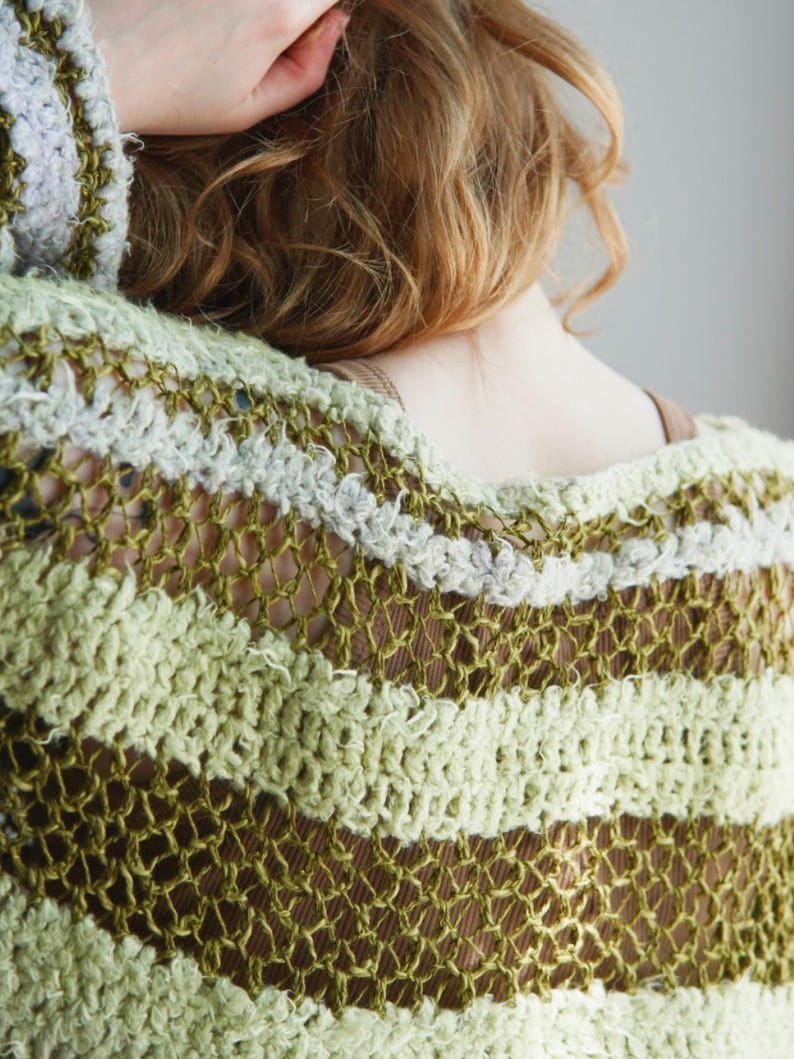 May include: A loose-knit crochet jumper featuring horizontal stripes in varying shades of olive green, light sage, and cream. The garment is constructed with an open, airy stitch pattern that creates a textured, semi-sheer appearance throughout.