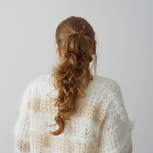May include: A long-sleeved, loose-knit jumper featuring horizontal stripes in alternating white and beige. The garment is crafted with a fuzzy, textured yarn that creates a soft, open-weave appearance throughout the entire piece.