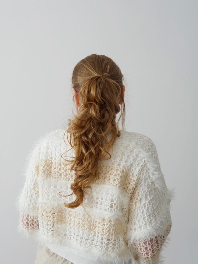 May include: A long-sleeved, loose-knit jumper featuring horizontal stripes in alternating white and beige. The garment is crafted with a fuzzy, textured yarn that creates a soft, open-weave appearance throughout the entire piece.