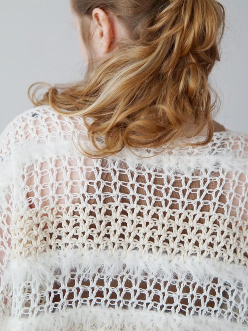 May include: A loose-knit crochet top featuring alternating horizontal bands of white and beige yarn. The garment displays a mix of open-work stitch patterns and textured, fuzzy yarn sections, creating a layered, semi-sheer appearance throughout.