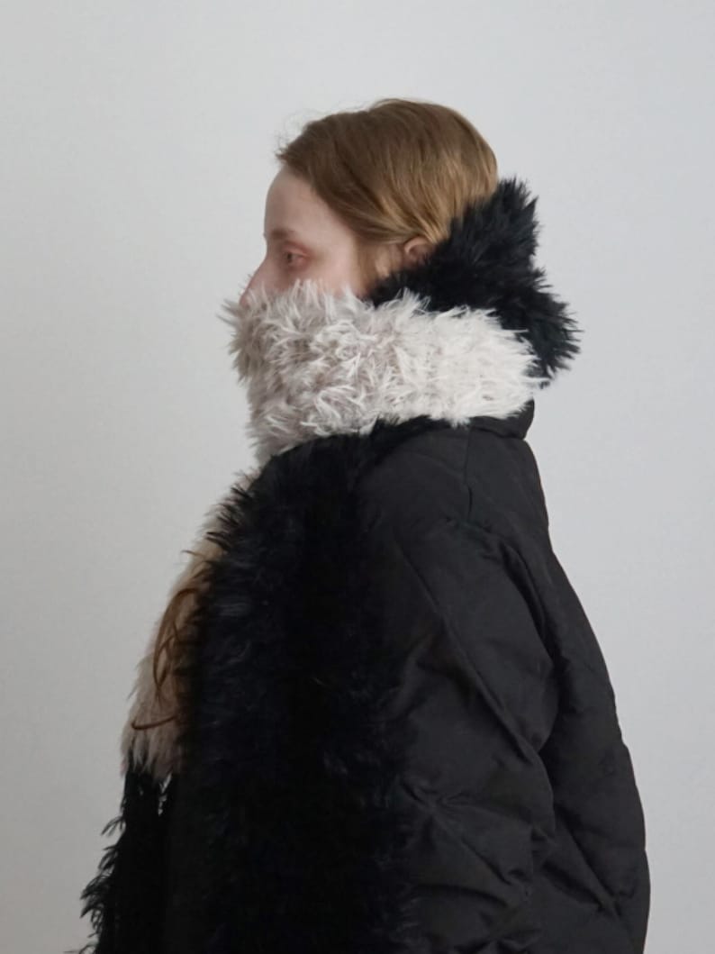 May include: A black quilted puffer jacket featuring a high collar and front panels adorned with long, shaggy faux fur in contrasting shades of cream and black. The textured fur trim extends from the neck down the front of the garment.