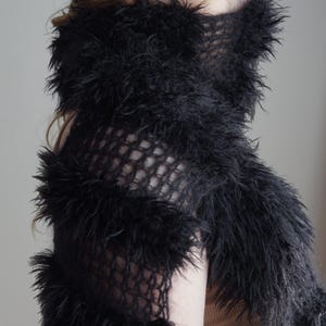 May include: A black scarf featuring a combination of open-knit mesh sections and dense, shaggy faux fur horizontal bands. The accessory is wrapped around the neck and lower face, showcasing a textured, layered appearance with long, soft fibers.