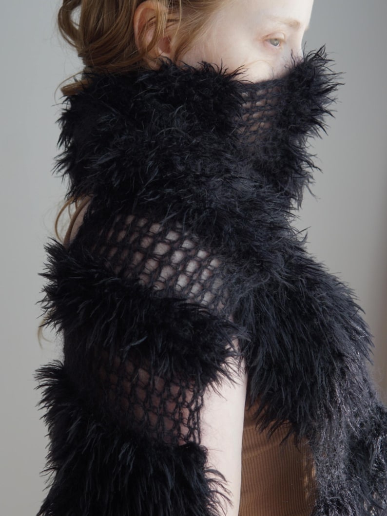 May include: A black scarf featuring a combination of open-knit mesh sections and dense, shaggy faux fur horizontal bands. The accessory is wrapped around the neck and lower face, showcasing a textured, layered appearance with long, soft fibers.
