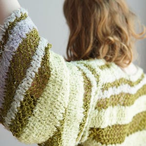 May include: A long-sleeved crochet jumper featuring horizontal stripes in shades of olive green, pale yellow, and light lavender. The garment is constructed with a combination of dense, textured stitches and open, airy mesh sections throughout.