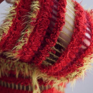May include: A textured knit garment featuring alternating horizontal bands of fuzzy red yarn and open-work yellow yarn. The fabric displays a distinct contrast between the dense, shaggy red sections and the airy, ladder-like yellow knit structure.