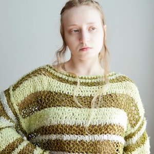 May include: A long-sleeved, loose-knit jumper featuring horizontal stripes in shades of light lime green, olive green, and white. The garment is constructed with a combination of textured, fuzzy yarn and an open, airy crochet stitch pattern.