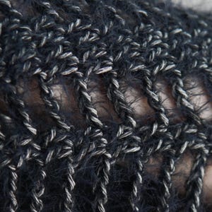 May include: A close-up view of a dark navy blue and silver metallic crochet fabric. The material features a fuzzy, textured yarn intertwined with a shimmering silver thread, creating an open, airy, and repeating geometric pattern throughout the textile.