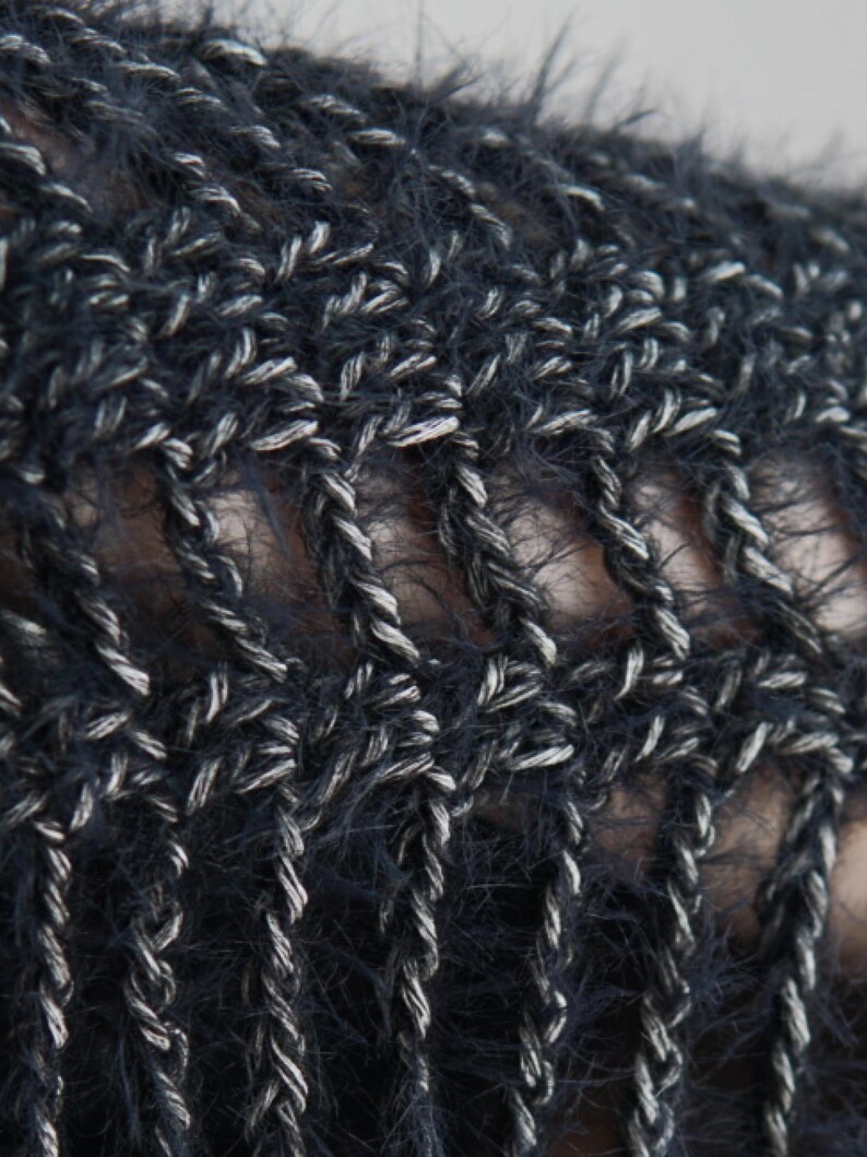 May include: A close-up view of a dark navy blue and silver metallic crochet fabric. The material features a fuzzy, textured yarn intertwined with a shimmering silver thread, creating an open, airy, and repeating geometric pattern throughout the textile.