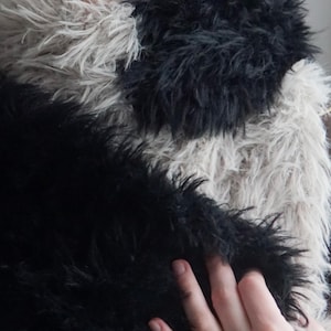 May include: A long, plush scarf featuring a color-blocked design with alternating sections of deep black and light beige faux fur. The texture is shaggy and dense, providing a thick, layered appearance across the entire length of the accessory.